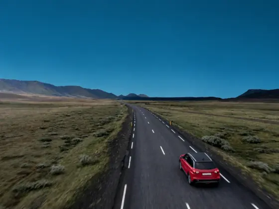 Red car travelling along a road through a mountainous landscape