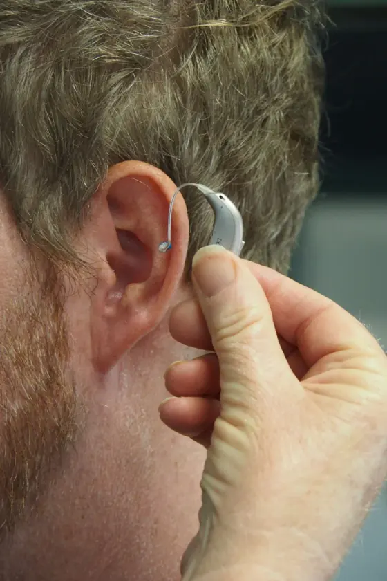 Person fitting a hearing aid behind their ear